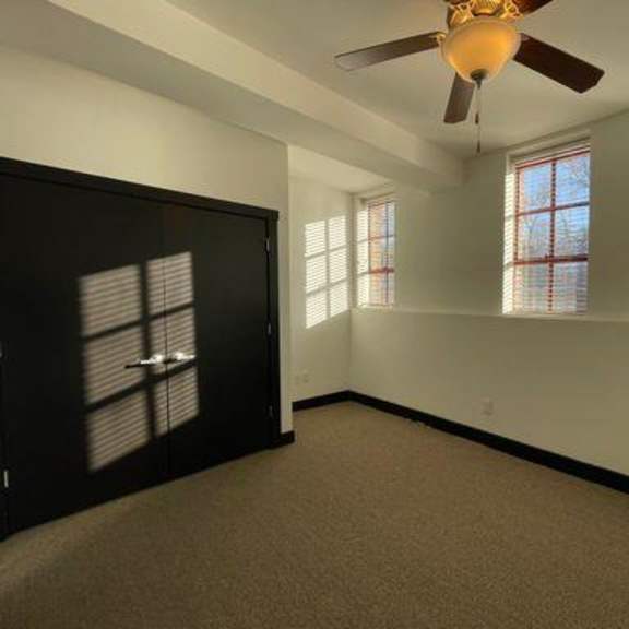a room with a ceiling fan and two windows.