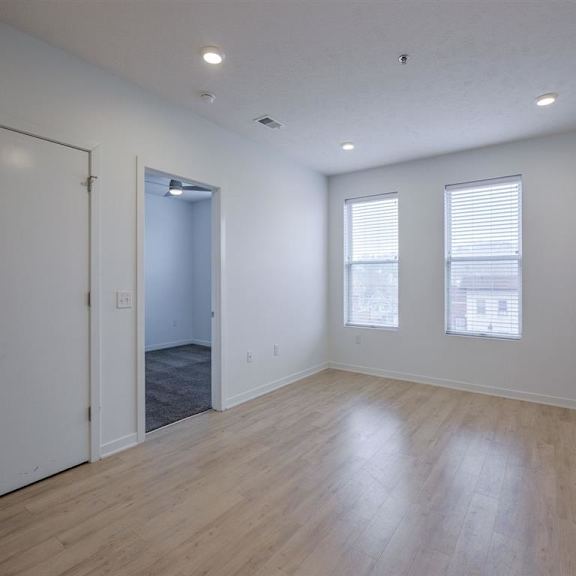 a room with white walls and wooden flooring, with a door on the left and a window on the right.