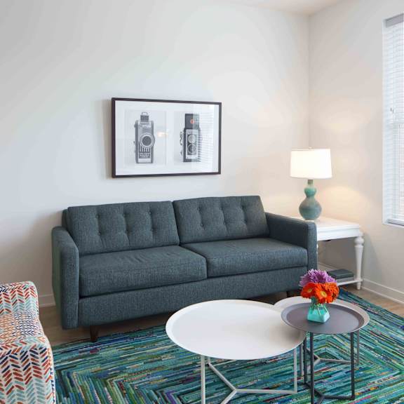 a grey sofa with a white table in front of it and a colorful rug on the floor.