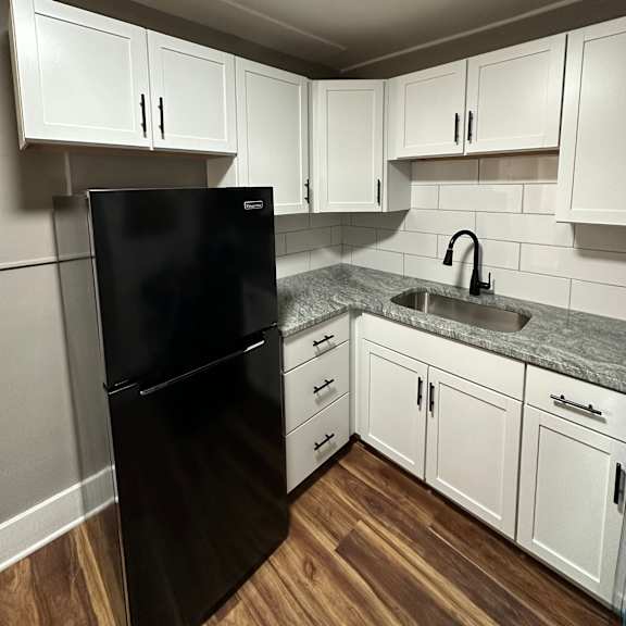 a black refrigerator stands in a kitchen with white cabinets.