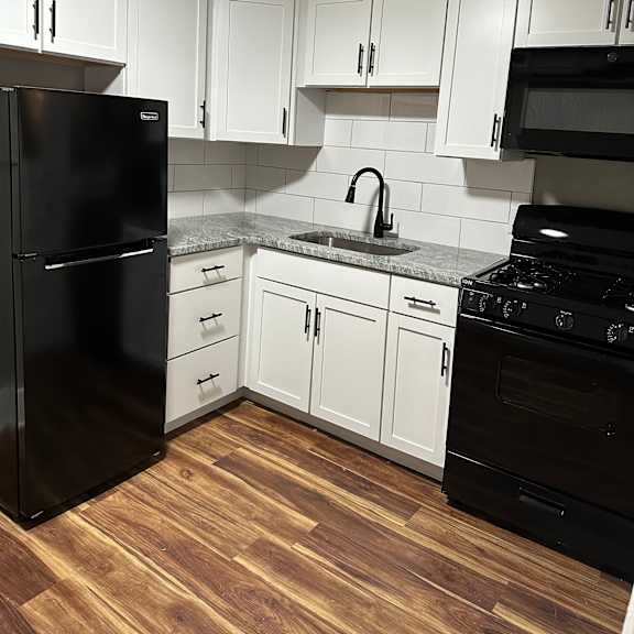 a black refrigerator stands in a kitchen with white cabinets.