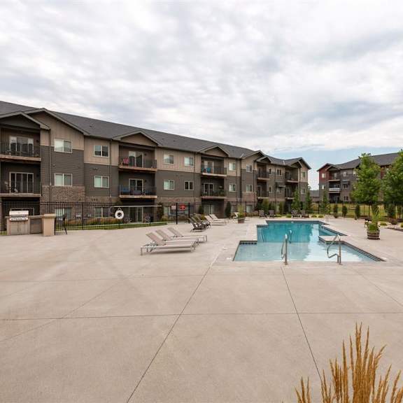 a large outdoor swimming pool surrounded by lounge chairs and apartment buildings.
