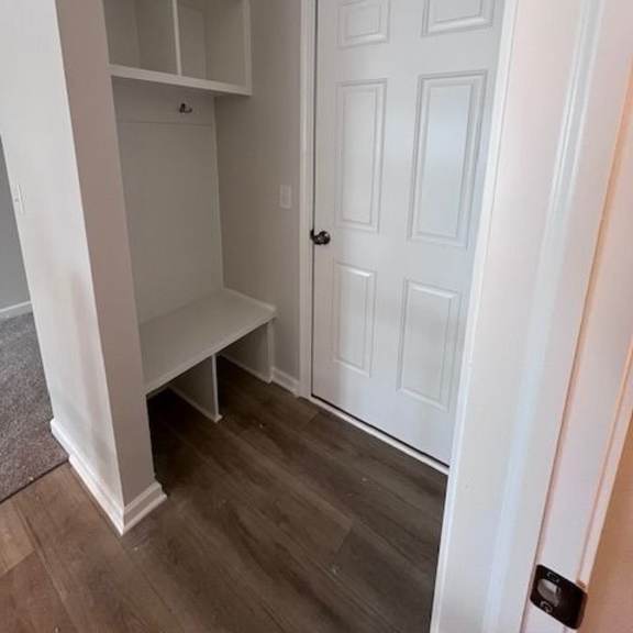 a white door is in a white room with a bench and shelves.