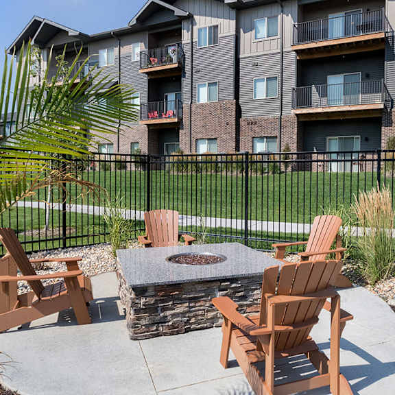 a patio with chairs and a fire pit in front of a brick building.
