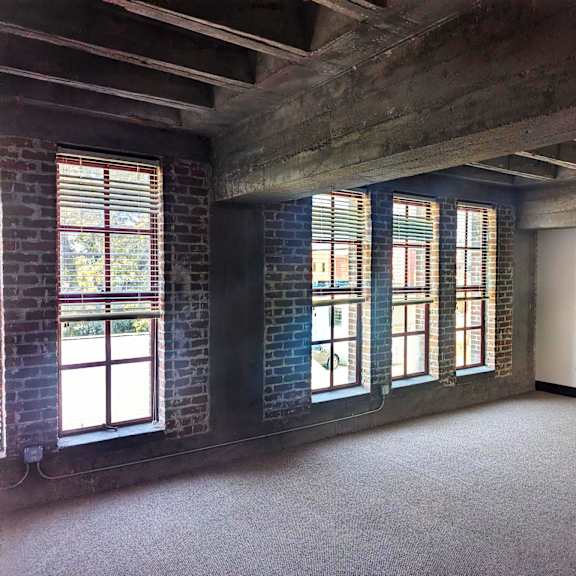 a room with a concrete ceiling and brick walls with windows.