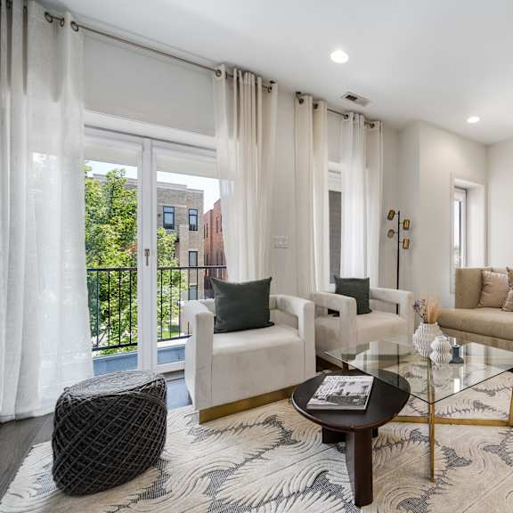 a living room with a white sofa, a black ottoman, and a glass coffee table.