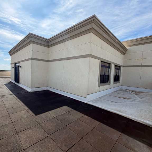 a large, empty patio area with a tiled floor and a building with a flat roof in the background.