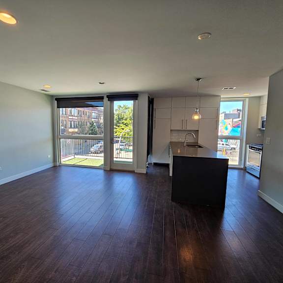 an empty living room with a kitchen and sliding glass doors