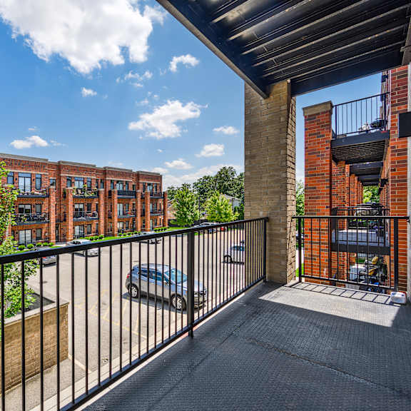 a balcony with a black railing overlooks a parking lot and a building.