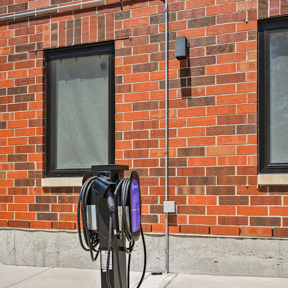 a black electric vehicle charging station is installed on a sidewalk in front of a red brick building.