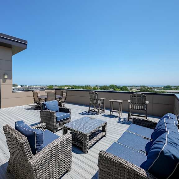 a rooftop deck with wicker furniture and a grill
