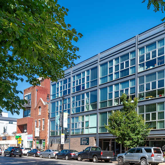 a modern glass building is situated on a street corner with cars parked in front.