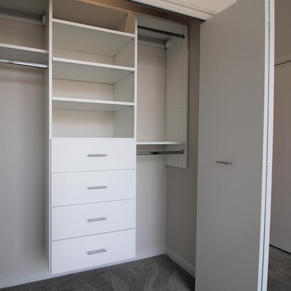 a walk in closet with white cabinets and drawers