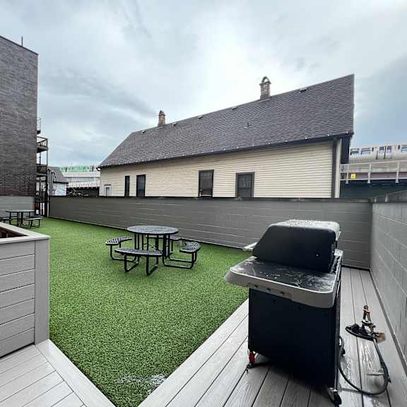 a roof deck with a grill and a picnic table on a green turf