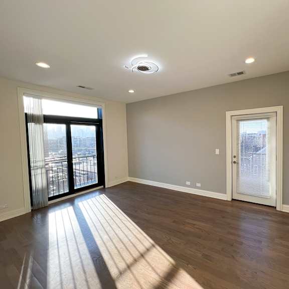 a spacious room with wooden flooring and a large window with a view of a cityscape.