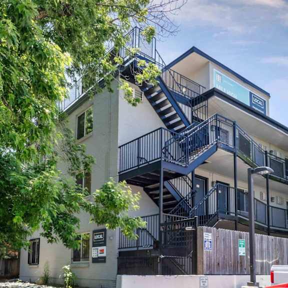 contemporary apartment building with black metal staircases, balconies, and mature trees surrounding the property at 1443 elizabeth in denver, co