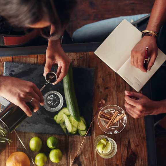 a person pouring wine into a bottle on a table with fruits and vegetables
