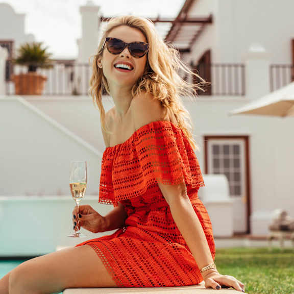 a woman in a red dress sitting by a pool holding a glass of wine