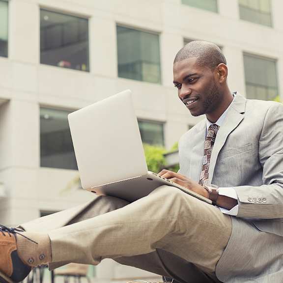 a man sitting on a bench using a laptop computer