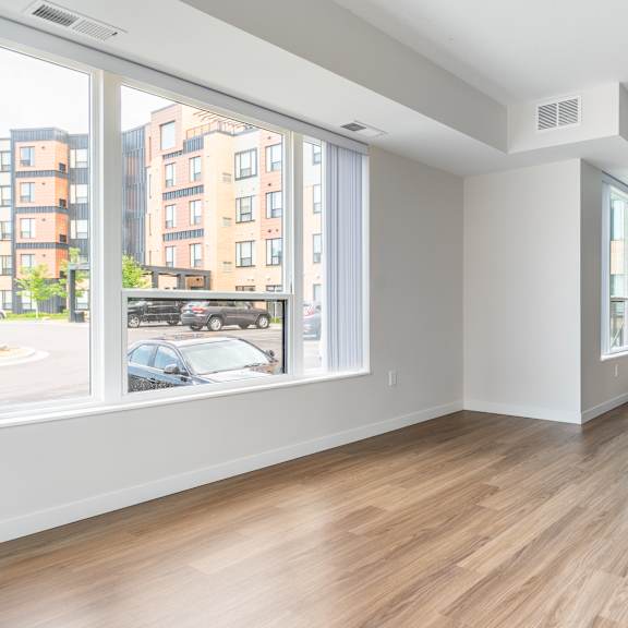 an empty living room with a large window and a kitchen in the background at sonder point 50+ apartments, brooklyn center, 55430