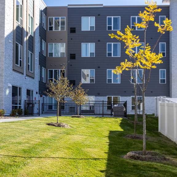 a courtyard with grass and trees in front of an apartment building