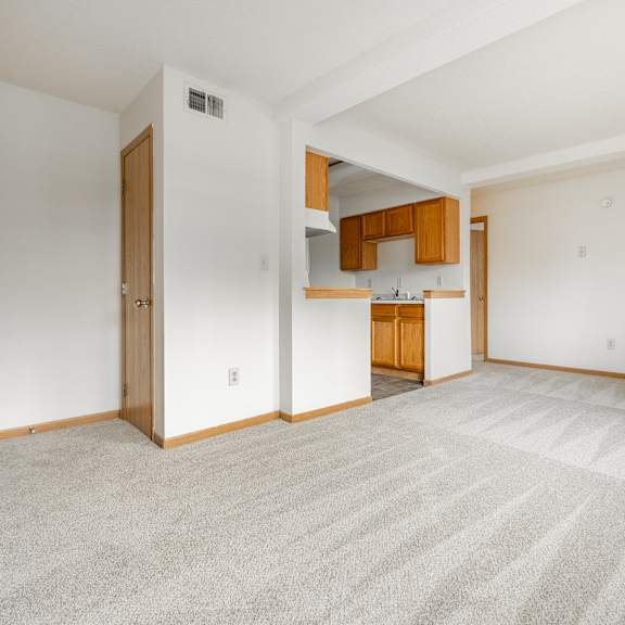 an empty living room and kitchen with white walls and carpet at ames lake neighborhood apartments, minnesota