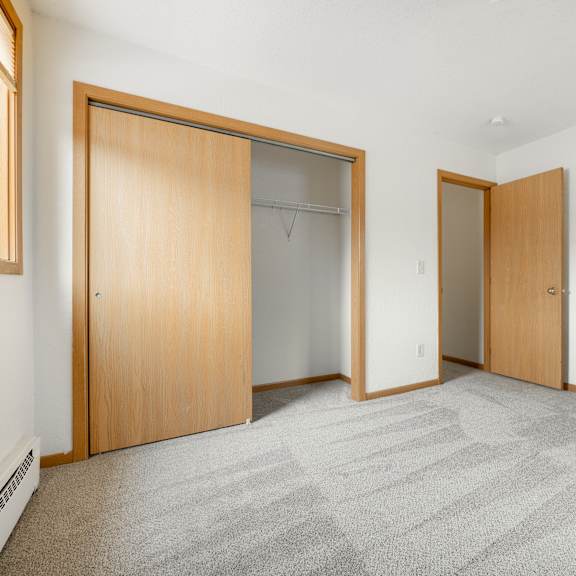 a bedroom with a carpeted floor and two closet doors at ames lake neighborhood apartments, st. paul, mn, 55106
