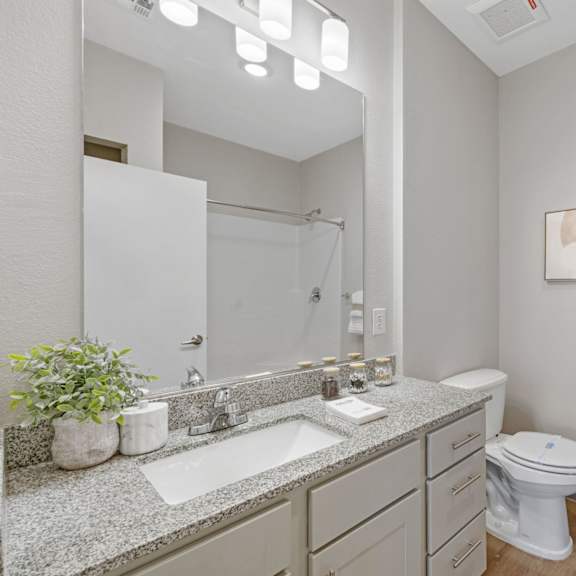 a bathroom with a toilet, sink, and mirror at copa flats apartments, apartments, maricopa, az