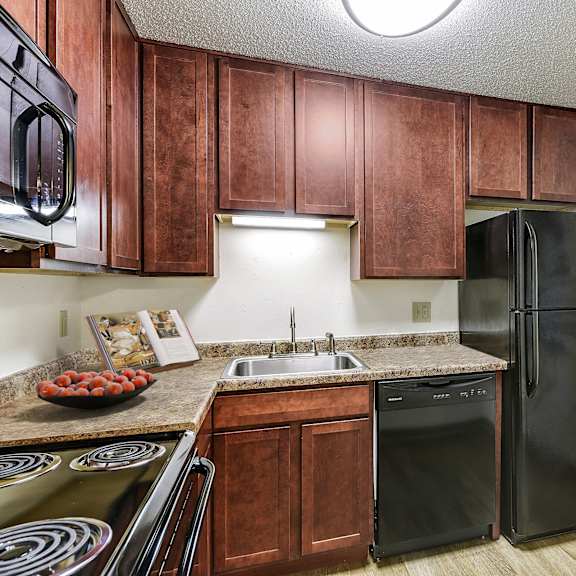 a kitchen with black appliances and wooden cabinets at pheasant park apartments, new hope, mn