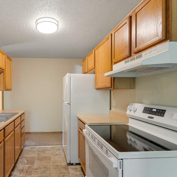 a kitchen with wooden cabinets and white appliances at ames lake neighborhood apartments, minnesota