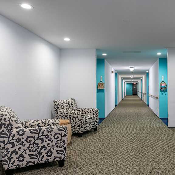 a long hallway with white and blue walls and a carpeted floor and some chairs at humboldt senior 55+ apartments, saint paul, 55107