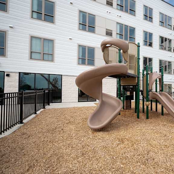 a playground with two slides and a chair in front of an apartment building at the landing at amber fields apartments, rosemount, minnesota