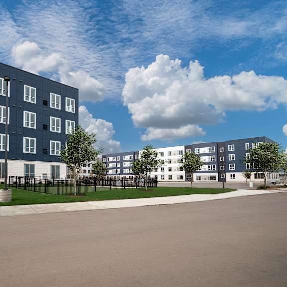 outside view of building with fenced dog park at the landing at amber fields apartments, minnesota