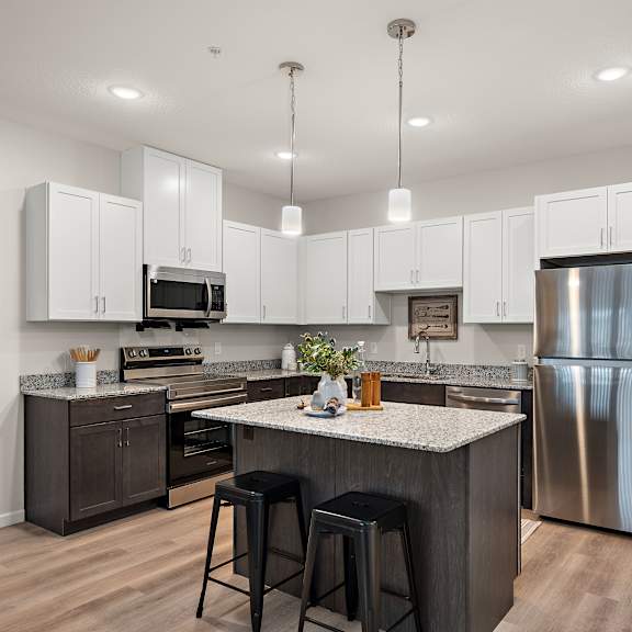 an open kitchen with a large island and stainless steel refrigerator at the landing at amber fields apartments, rosemount, minnesota