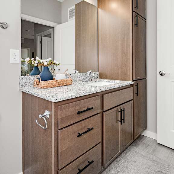 bathroom vanity with tall storage cabinet and mirror at reserve at settlers ridge apartments, woodbury