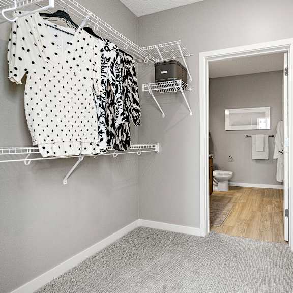 a walk in closet with clothes hanging and shelves with storage boxes.