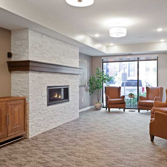 a living room with a fireplace and chairs at sonder point 50+ apartments, brooklyn center