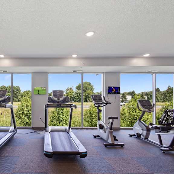 a gym with cardio equipment and windows with a view of a field