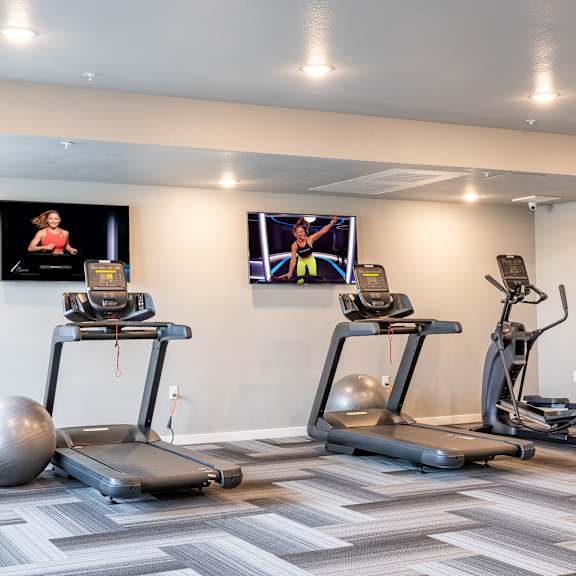 two treadmills and exercise balls in a gym with televisions at technology park apartments, minnesota