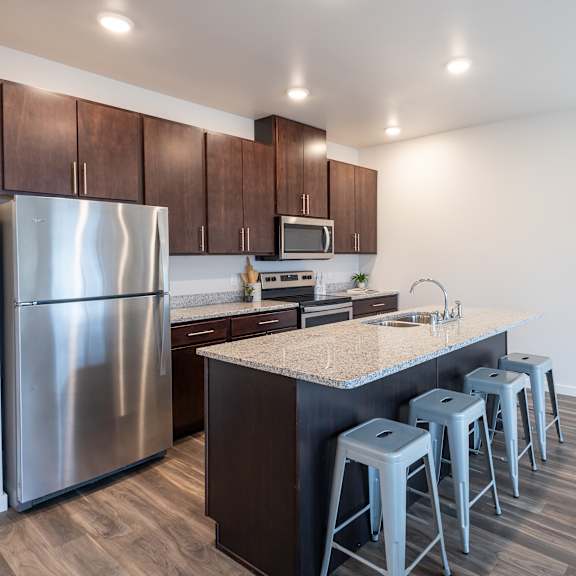 a kitchen with a large island with bar stools and stainless steel refrigerator at technology park apartments, rochester, mn