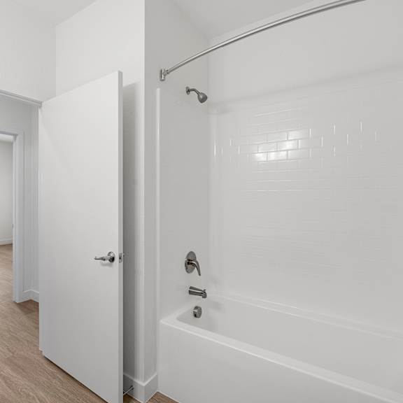 a white bathroom with a tub and a door leading to a hallway.