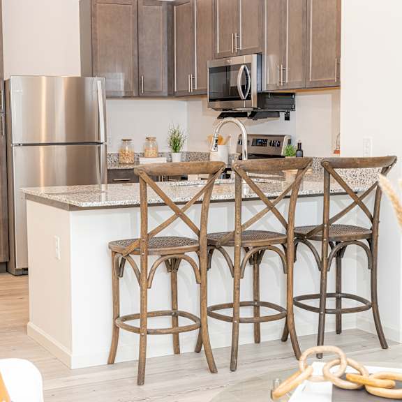 a kitchen with an island with three bar stools and a stainless steel refrigerator