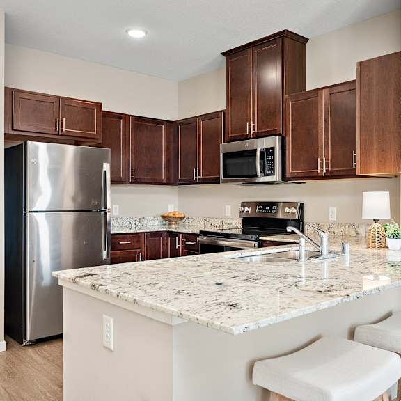 a kitchen with a granite countertop and white stools at the winslow 62+ apartments, west st paul