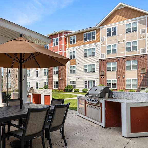 a patio with an umbrella and a table with chairs and a grill at the winslow 62+ apartments, minnesota
