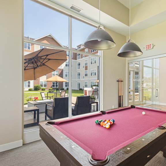 a pool table in a clubhouse with two lights hanging over it at the winslow 62+ apartments, west st paul, minnesota