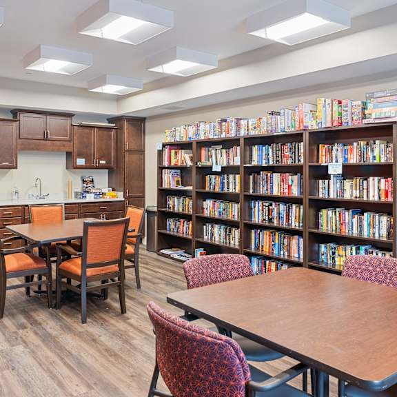 a library with tables and chairs and a kitchen and library shelves at the winslow 62+ apartments, west st paul, minnesota