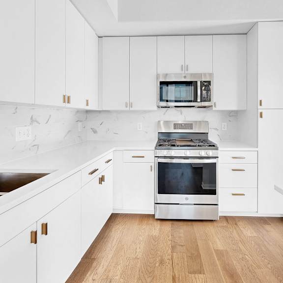 Thumbnail 8 of 12 A modern kitchen with white cabinets and a wooden floor.