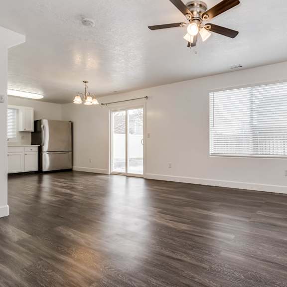 an empty living room with a ceiling fan and a kitchen
