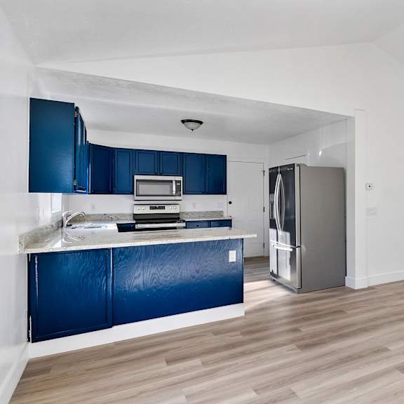 an empty kitchen with blue cabinets and a stainless steel refrigerator