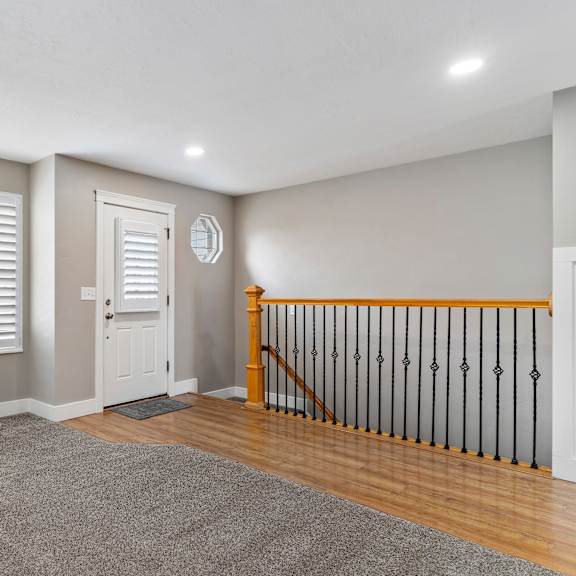 a room with a white door, a window with white shutters, and a wooden staircase.